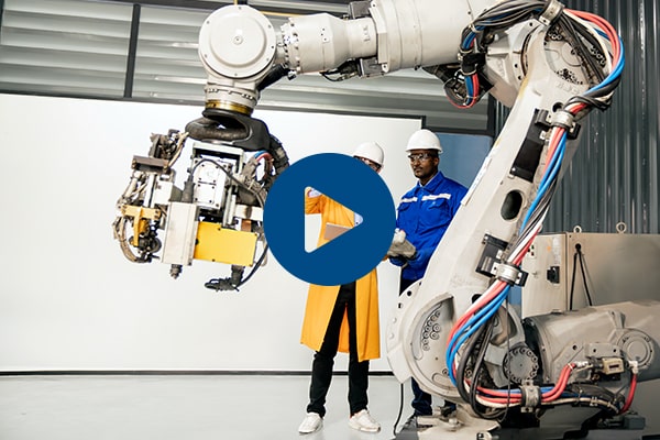 Two industrial workers standing behind a large robotic arm